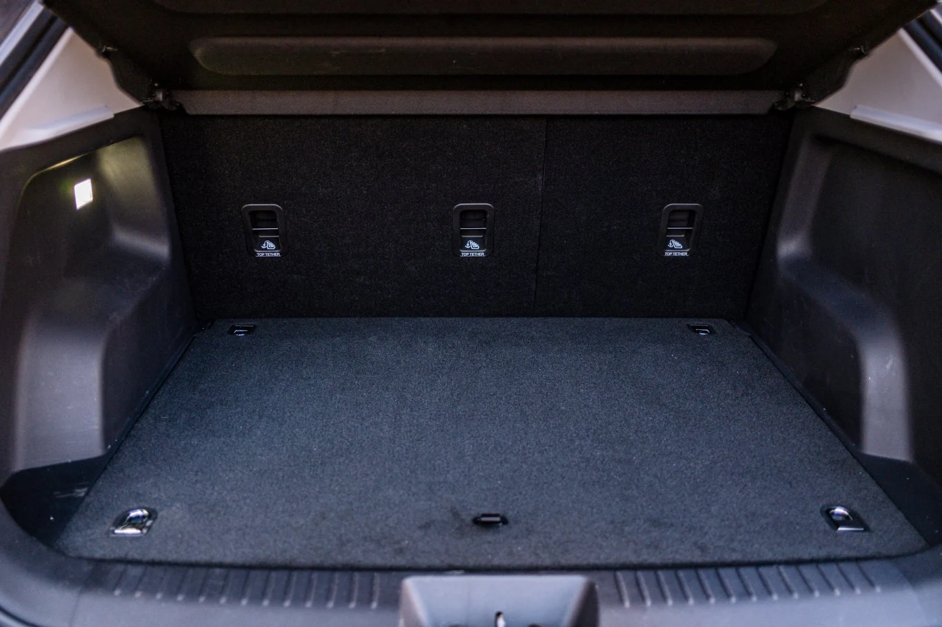 przestronny bagażnik samochodu z ciemną wykładziną, trzema zaczepami mocującymi na tylnej ścianie oraz oświetleniem po lewej stronie