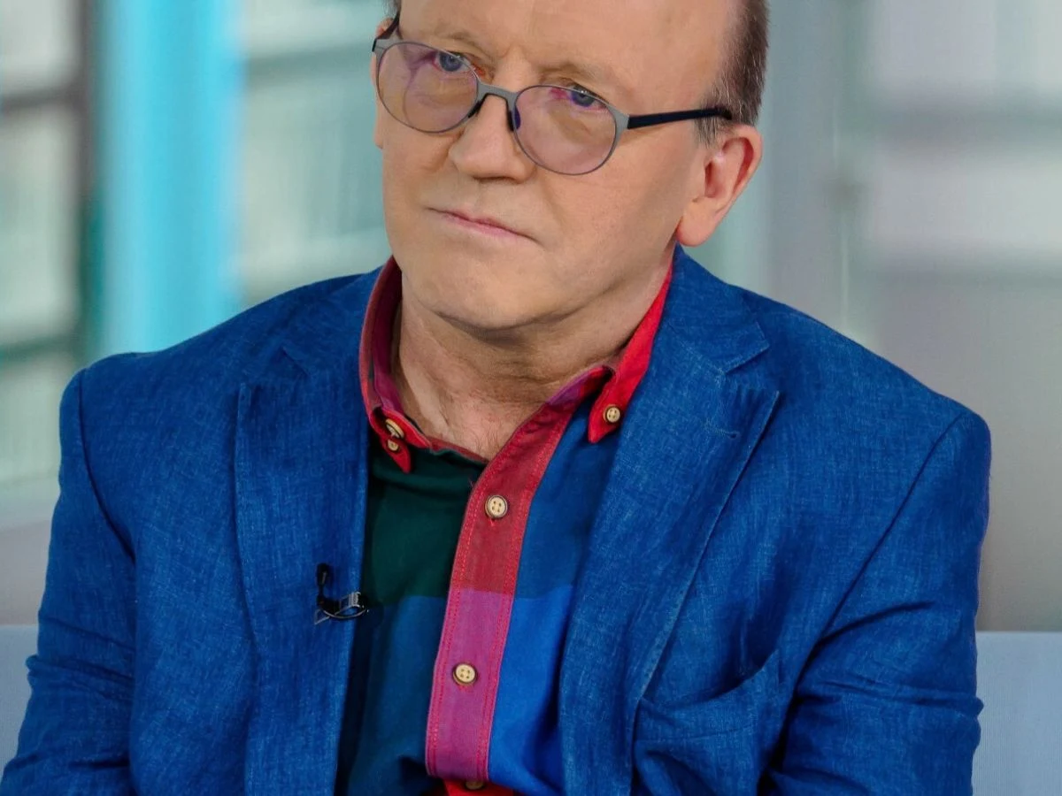 Artur Barciś Artur Barciś w okularach, niebieskiej marynarce i koszuli w kratę, siedzi w jasnym, nowoczesnym wnętrzu.