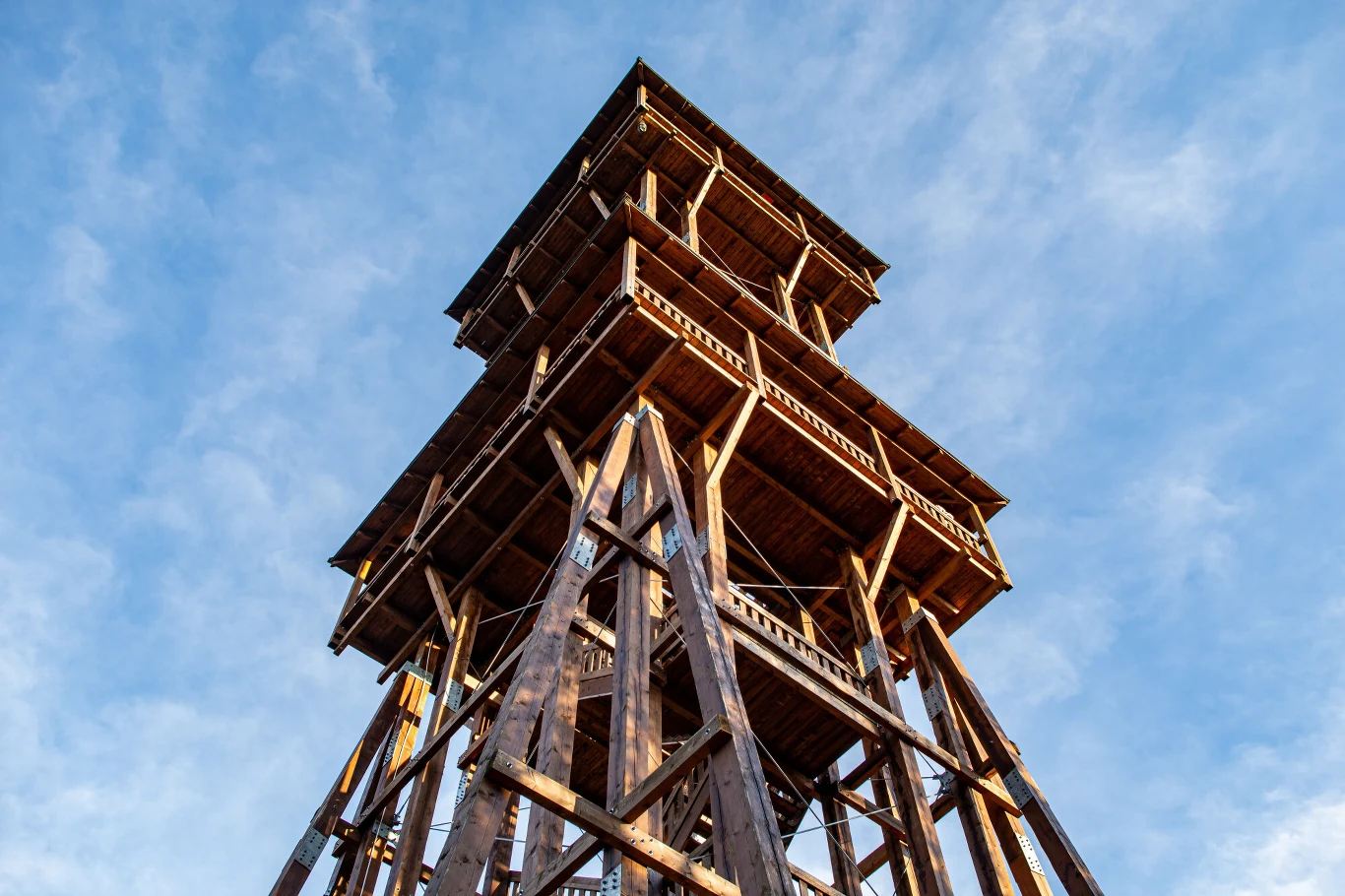 drewniana wieża widokowa z solidnymi podporami i dwoma tarasami obserwacyjnymi, sfotografowana z dołu na tle jasnego, lekko zachmurzonego nieba