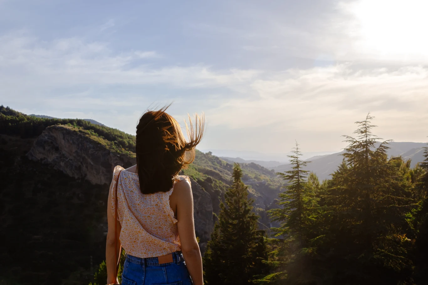 Wypad w Bieszczady na Wielkanoc to strzał w dziesiątkę Młoda kobieta stoi tyłem, patrząc na górski krajobraz otoczony gęstymi drzewami iglastymi, przy jasnym, słonecznym niebie.