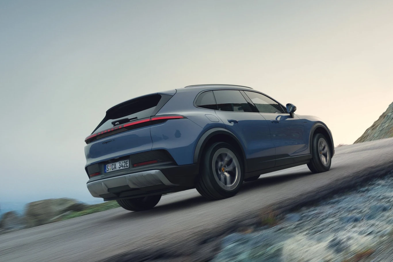 niebieski SUV o nowoczesnym designie jedzie pod górę po asfaltowej drodze, otoczony górskim krajobrazem i jasnym, lekko zamglonym niebem