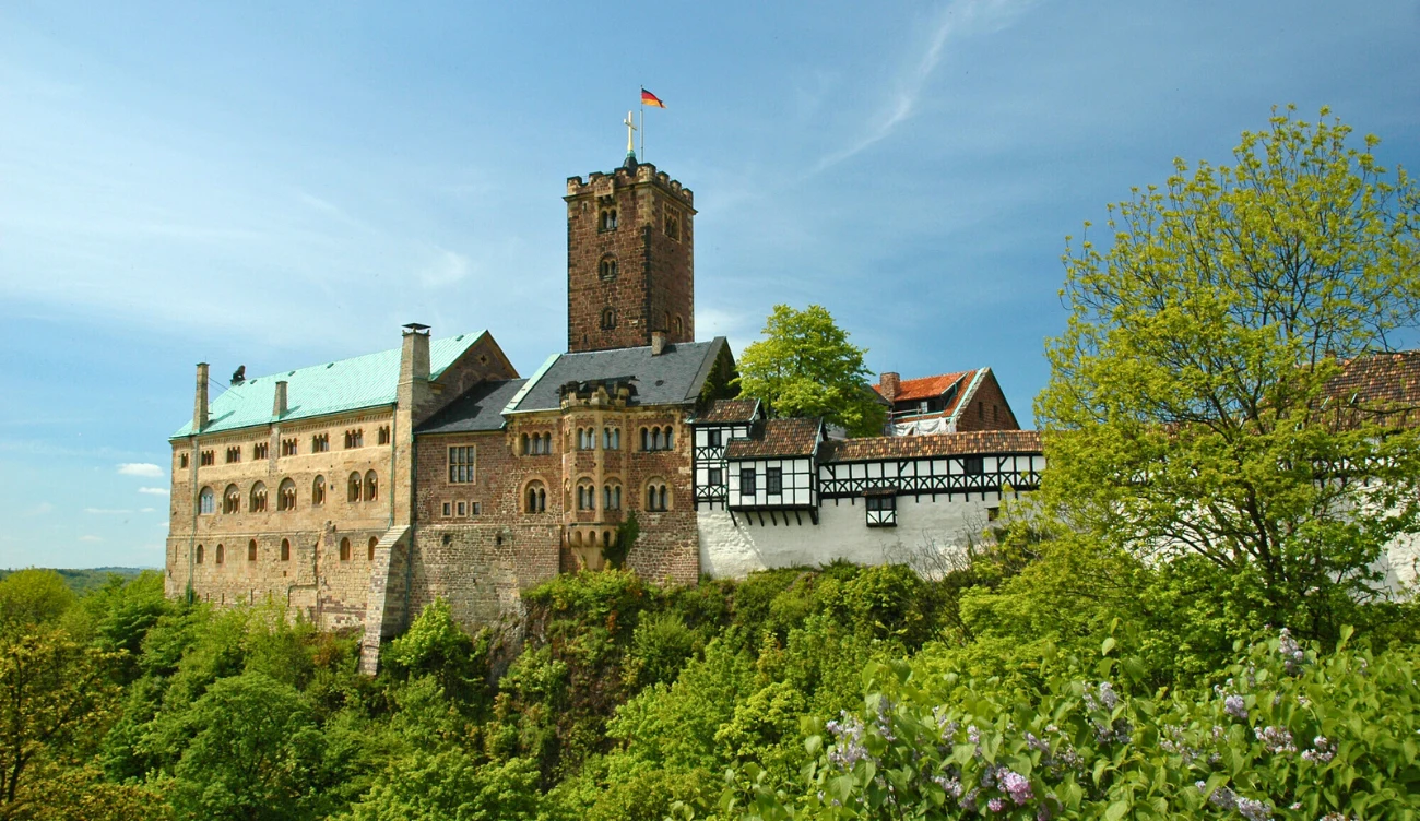 Z czego słynie zamek Wartburg? Zamek Wartburg – masywna kamienna twierdza z prostokątną wieżą, otoczona drzewami, na tle nieba