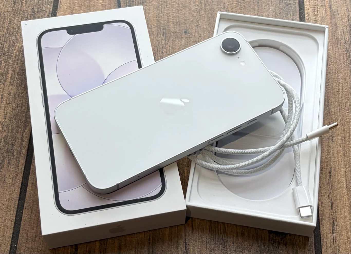 Zawartość opakowania smartfona iPhone 17e. biały smartfon z pojedynczym aparatem leżący na otwartym pudełku, obok widoczny zwinięty kabel USB-C