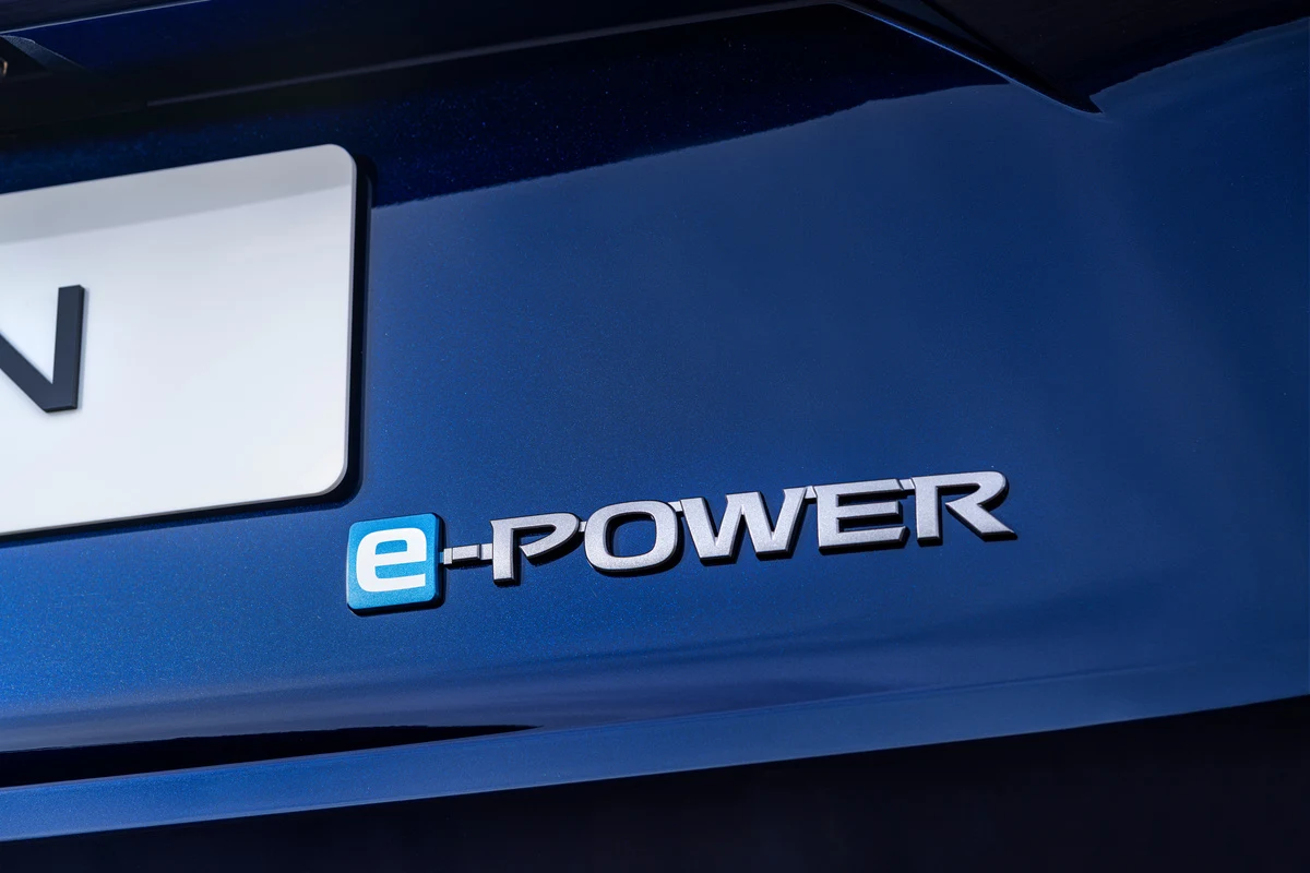 Błękitny napis e-POWER umieszczony na tylnej części nadwozia samochodu w ciemnoniebieskim kolorze, obok fragmentu tablicy rejestracyjnej.