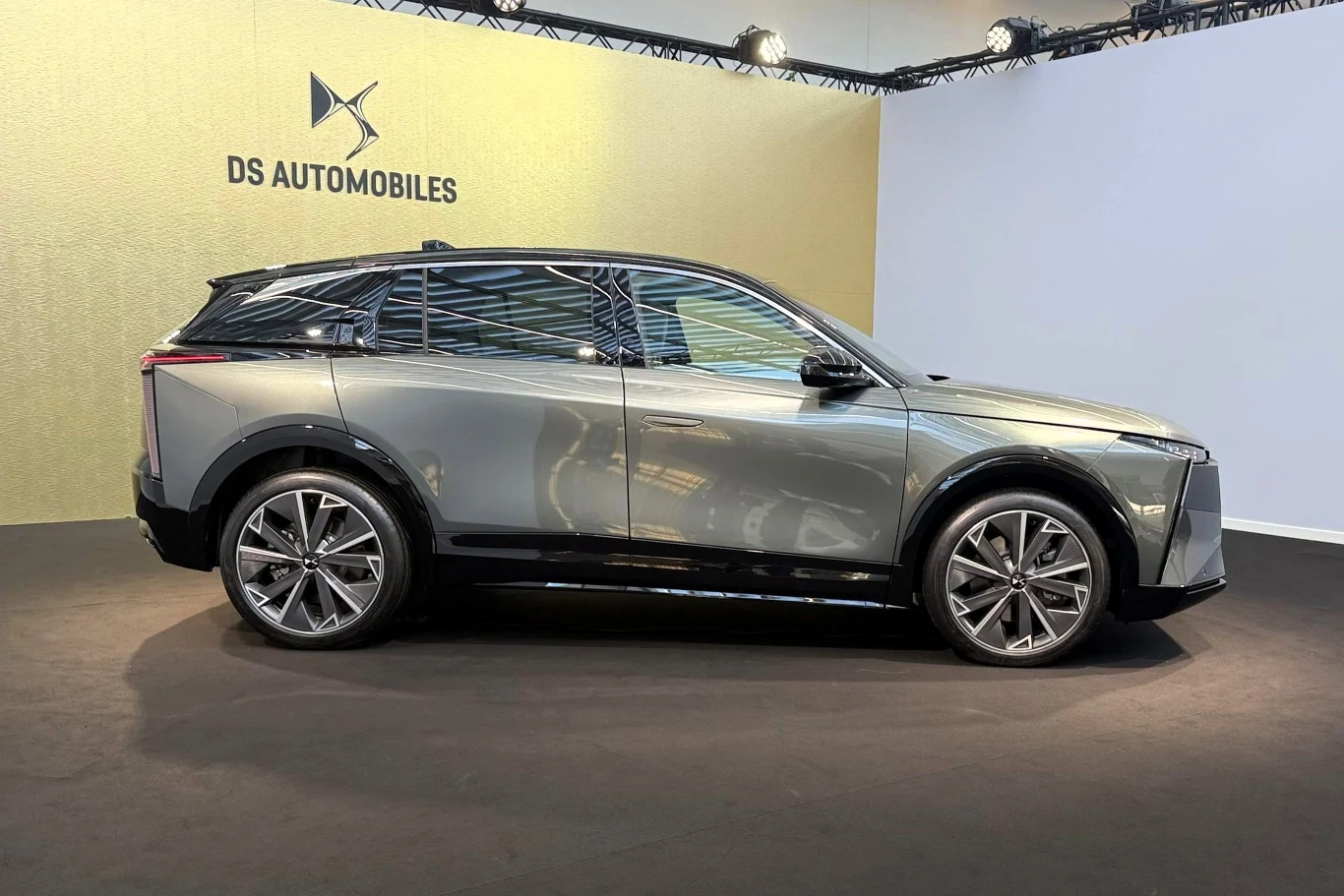Nowoczesny samochód SUV w kolorze srebrnym o dynamicznej sylwetce, dużych kołach i eleganckich, czarnych elementach wykończenia, stojący na ekspozycji przed złotą ścianą z logo DS Automobiles.