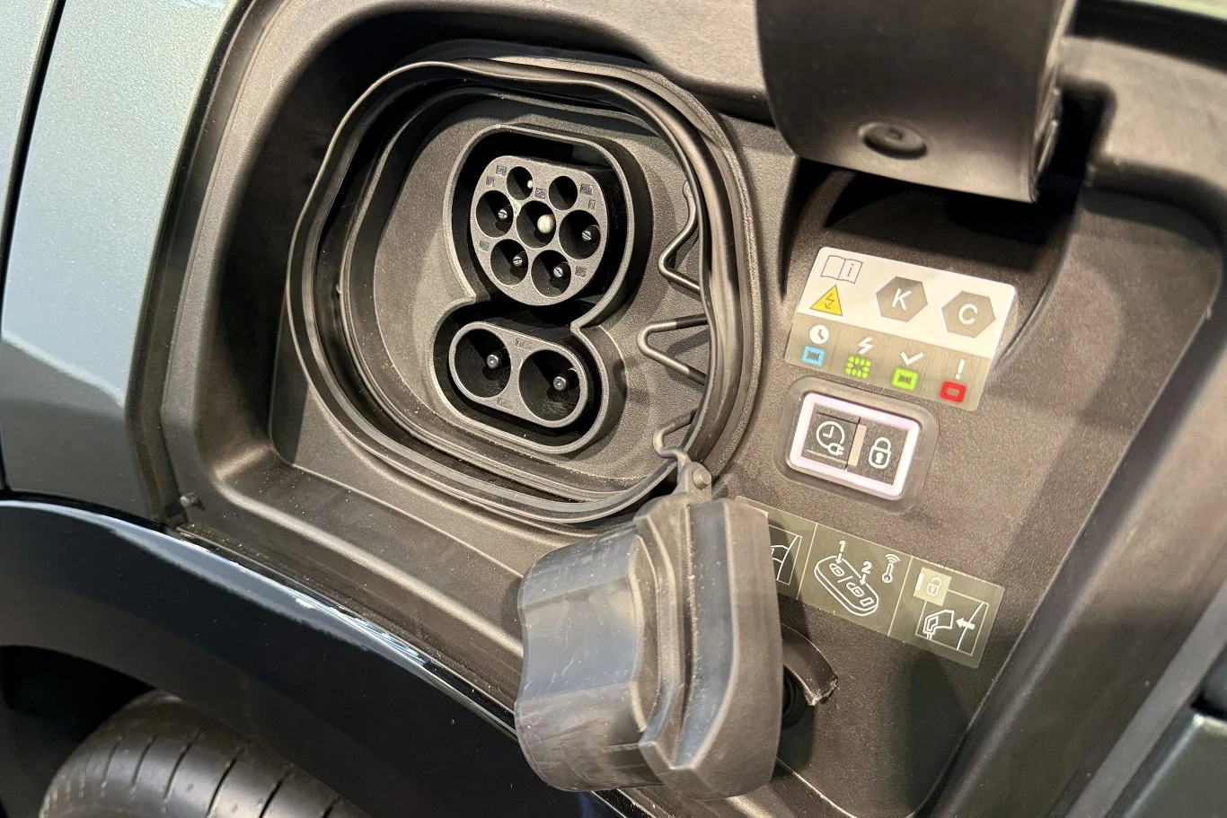 gniazdo ładowania samochodu elektrycznego typu CCS z otwartą klapką oraz zestawem ikon informacyjnych i wskaźników obok gniazda