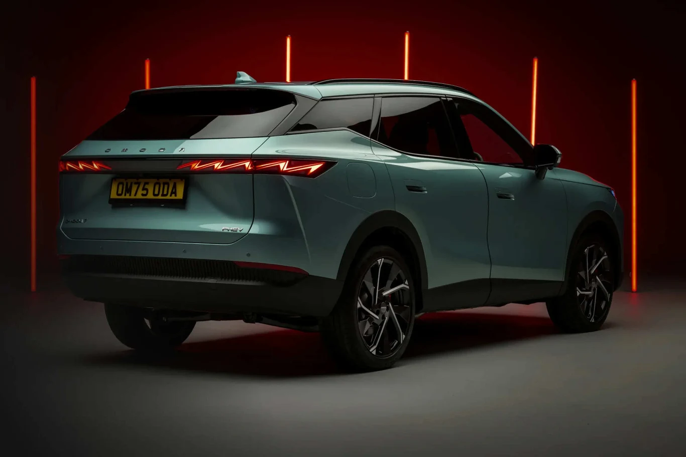 jasnoniebieski nowoczesny SUV z czarnymi detalami i dynamiczną linią nadwozia, efektowne tylne światła w kształcie litery Y, brytyjska tablica rejestracyjna, w tle pionowe czerwone neony podkreślające sylwetkę pojazdu