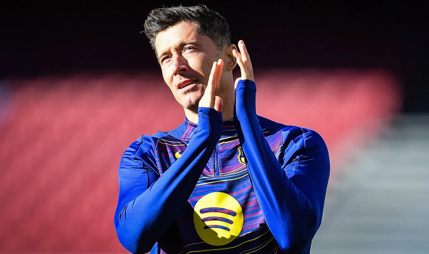 Robert Lewandowski Robert Lewandowski w koszulce FC Barcelony z logo Spotify bije brawo na tle czerwonego stadionu.
