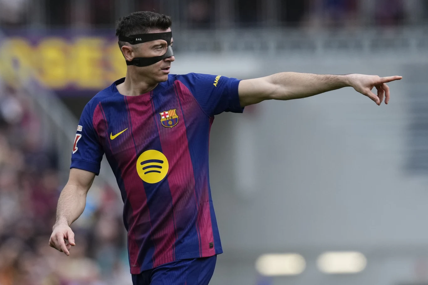 piłkarz w koszulce FC Barcelony z czarną opaską na twarzy energicznie wskazuje kierunek, koncentrując się na sytuacji boiskowej