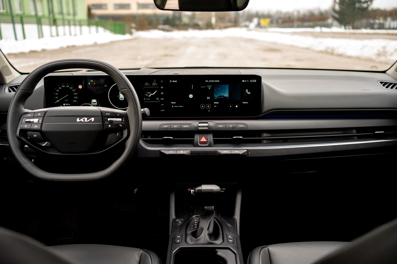 kokpit nowoczesnego samochodu marki Kia z cyfrowym zestawem wskaźników, dużym ekranem multimedialnym na środku deski rozdzielczej oraz minimalistycznym panelem sterowania klimatyzacją i przyciskami pod ekranem