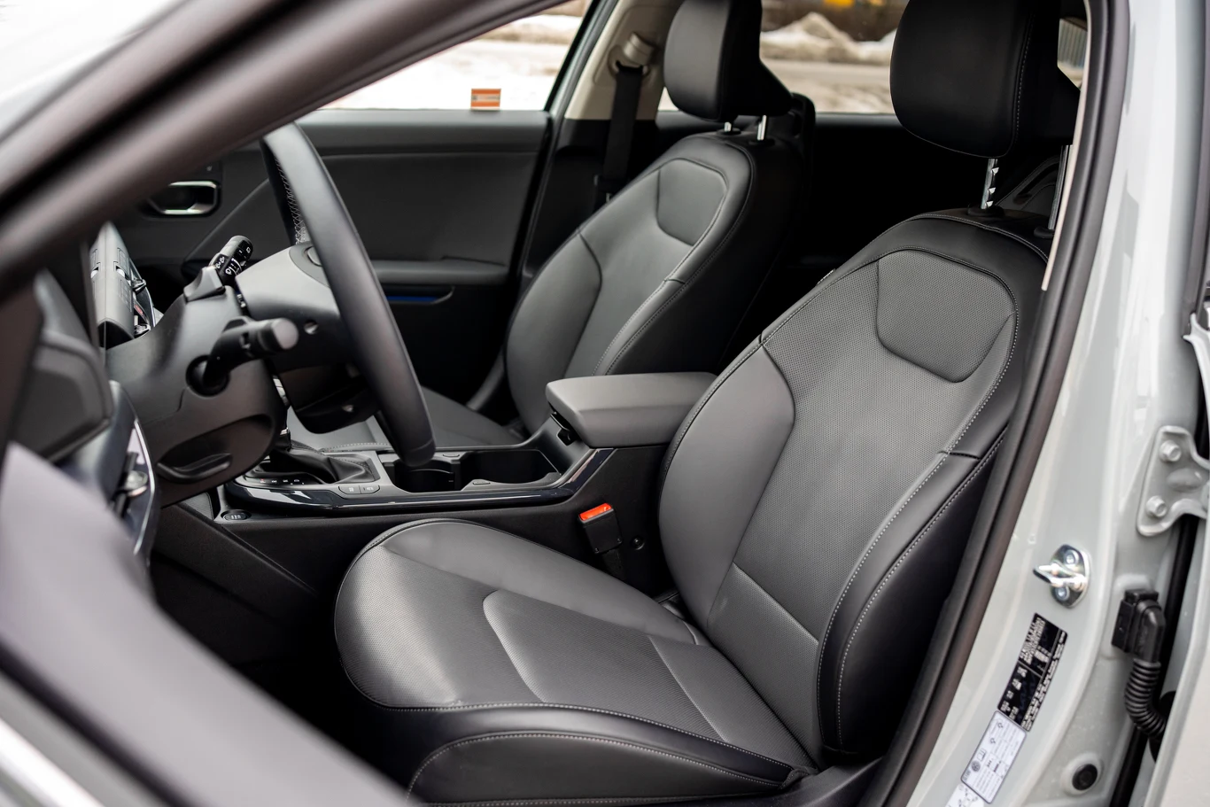 czarne, skórzane fotele samochodowe z wyraźnymi przeszyciami, nowoczesna deska rozdzielcza z dużym ekranem dotykowym i elegancką konsolą środkową, jasna tapicerka drzwi oraz automatyczna skrzynia biegów