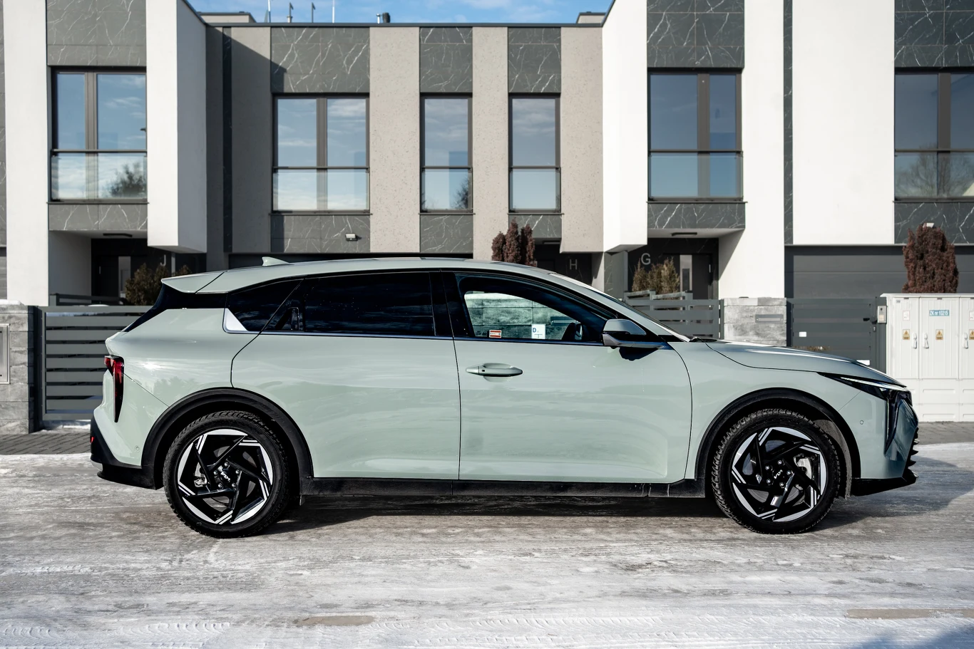 jasny nowoczesny samochód typu SUV zaparkowany przed szeregiem współczesnych budynków mieszkalnych, widok z boku podkreślający czarne felgi, opływowy kształt nadwozia i przyciemnione szyby