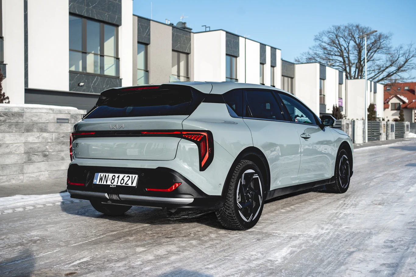 jasnoszary nowoczesny samochód typu hatchback z czarnym dachem oraz czarnymi akcentami, stojący na zaśnieżonej ulicy wśród nowoczesnych budynków mieszkalnych