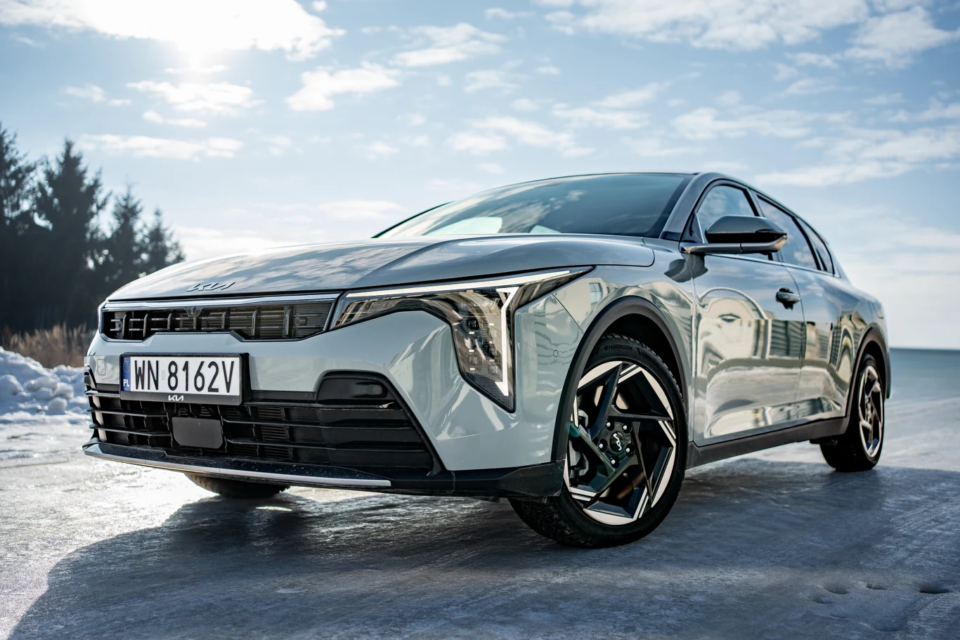 nowoczesny, srebrny samochód osobowy o futurystycznym designie z charakterystycznymi reflektorami w kształcie litery L, widoczny z niskiej perspektywy na tle błękitnego nieba i asfaltowej jezdni