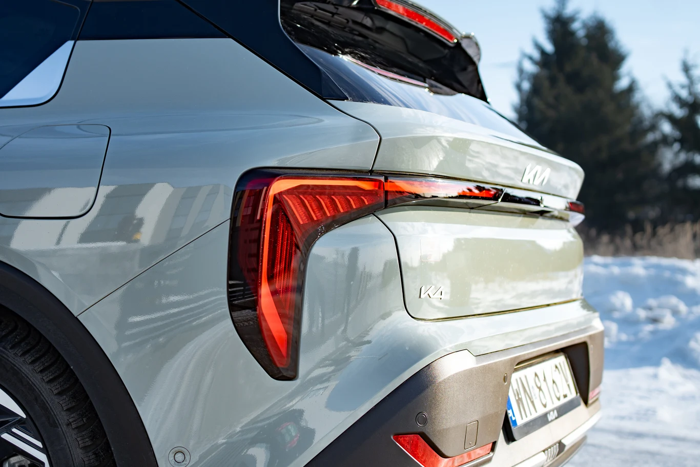 tylny fragment srebrnego samochodu marki Kia z nowoczesnymi, pionowymi światłami LED oraz widocznym logo na klapie bagażnika, w tle zimowy krajobraz z drzewami