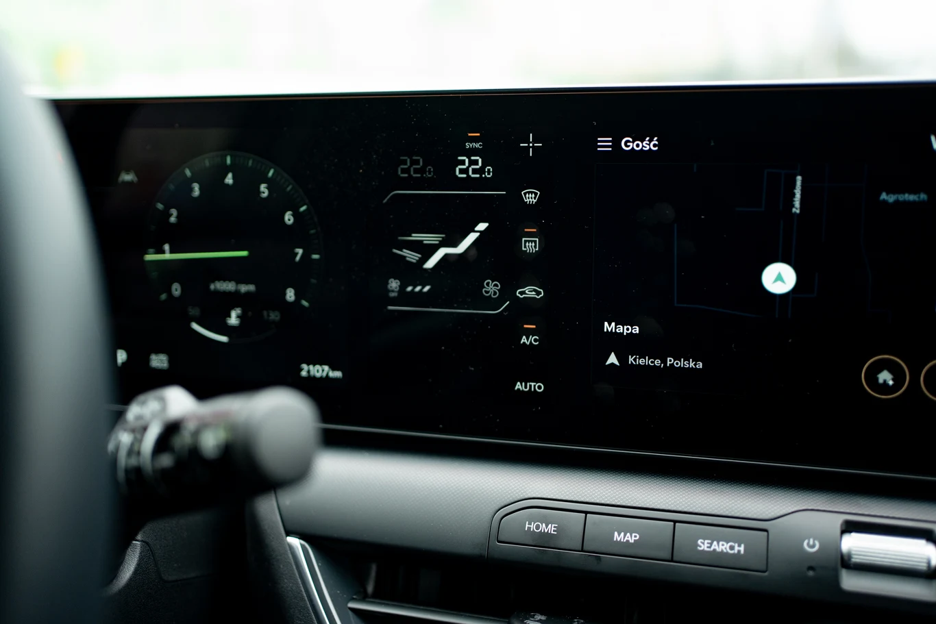 nowoczesny cyfrowy kokpit samochodu z wyświetlaczem zawierającym prędkościomierz, ustawienia klimatyzacji, nawigację z mapą lokalizacji oraz rozbudowane menu sterowania