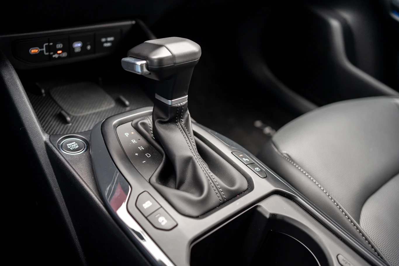 konsola środkowa samochodu z drążkiem automatycznej skrzyni biegów, przyciskami sterującymi oraz przyciskiem uruchamiania silnika, otoczona skórzaną tapicerką