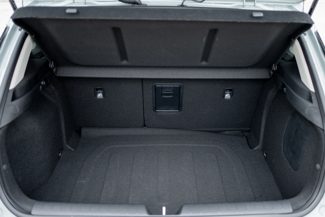 otwarty i pusty bagażnik samochodu osobowego, wyłożony czarną tapicerką, z widocznym schowkiem w tylnej części oraz uchwytami po bokach