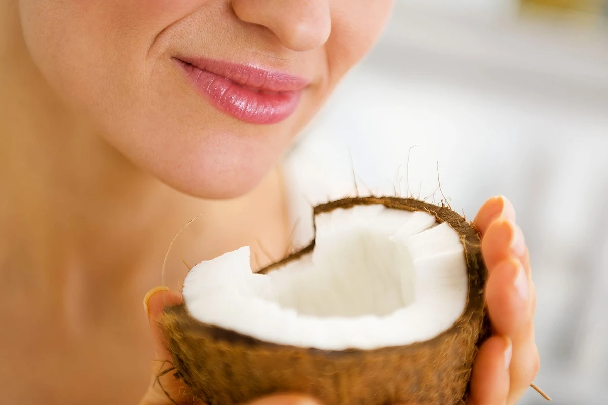 Woda kokosowa spożywana w nadmiarze może być szkodliwa uśmiechnięta kobieta trzyma w dłoniach połówkę kokosa, zbliżając ją do ust