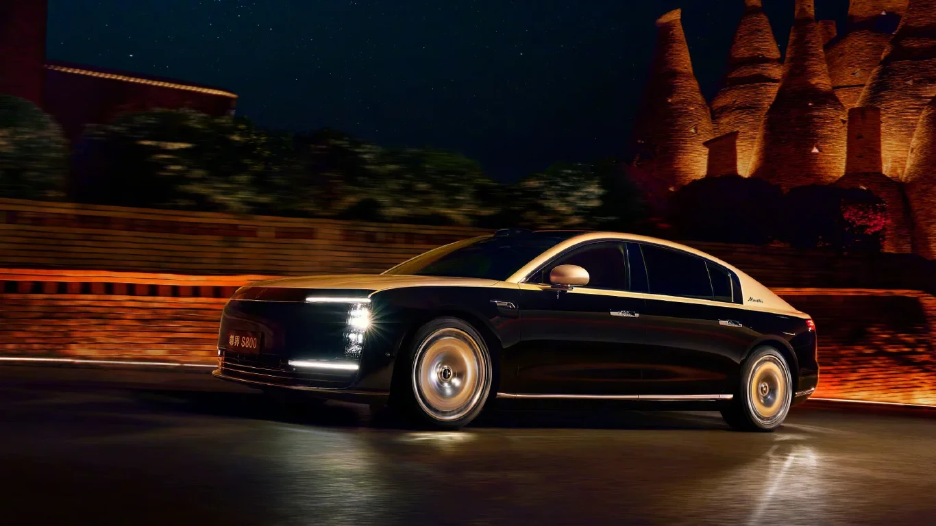 Czarny luksusowy sedan w ruchu na oświetlonej ulicy nocą, z charakterystycznym, nowoczesnym designem i reflektorami led, na tle podświetlonych zabytkowych murów i wież.