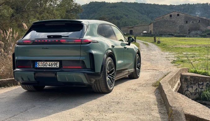 zielony nowoczesny SUV z przyciemnianymi szybami i sportowymi felgami stoi na wąskiej drodze prowadzącej w stronę kamiennego gospodarstwa, otoczonego zielonymi łąkami i wzgórzami porośniętymi lasem