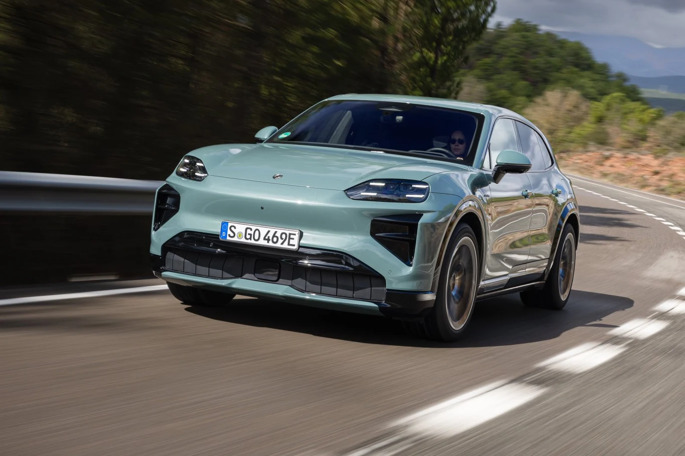 nowoczesny SUV o sportowej sylwetce w jasnozielonym kolorze jadący dynamicznie po łuku drogi, z czarnymi detalami nadwozia oraz charakterystycznym, agresywnym przodem, otoczony bujną zielenią i niskimi wzgórzami w tle