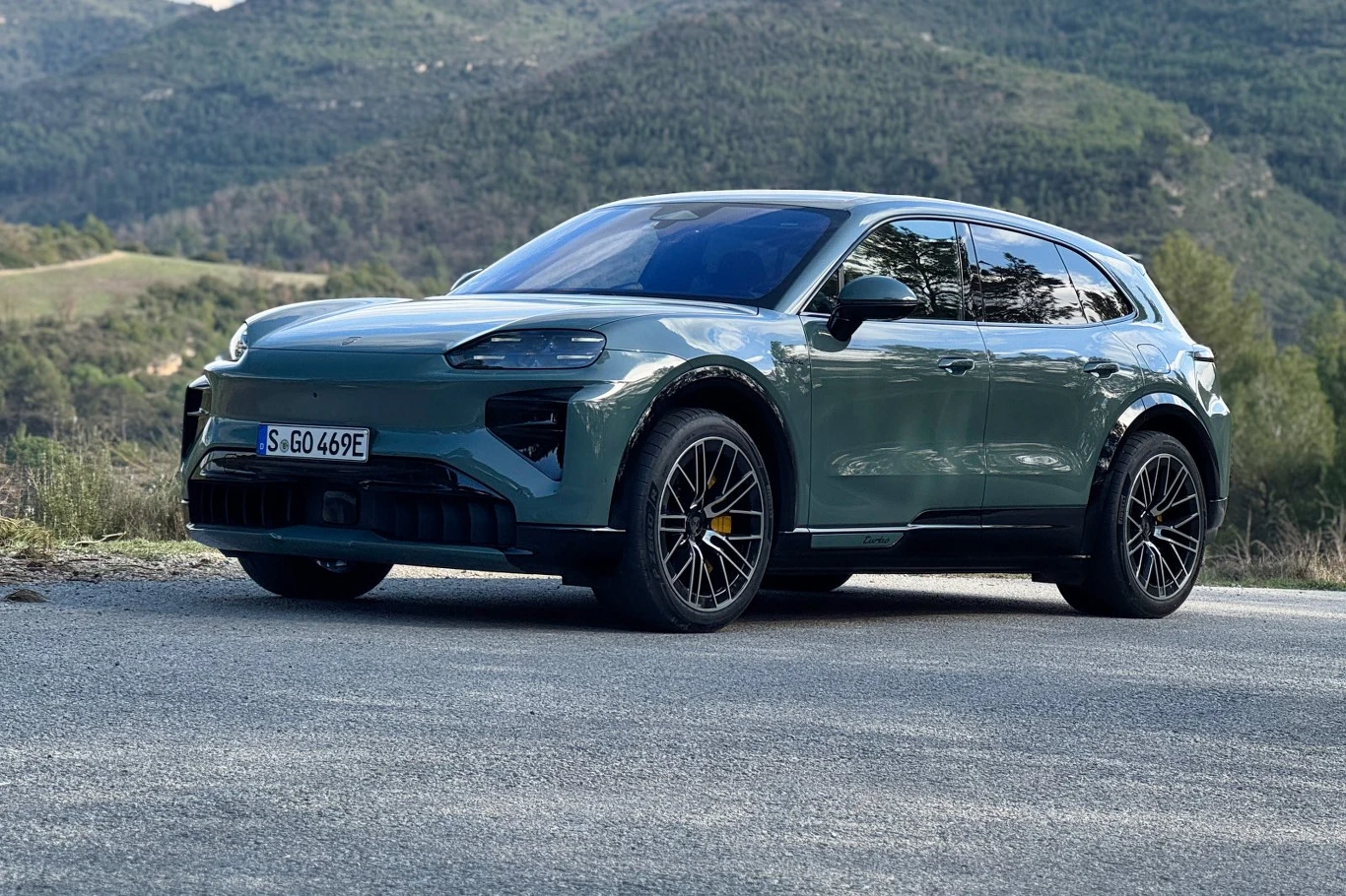 zielony, luksusowy SUV elektryczny o agresywnej stylistyce, masywnych felgach i czarnych wstawkach nadwozia stojący na tle zielonych wzgórz