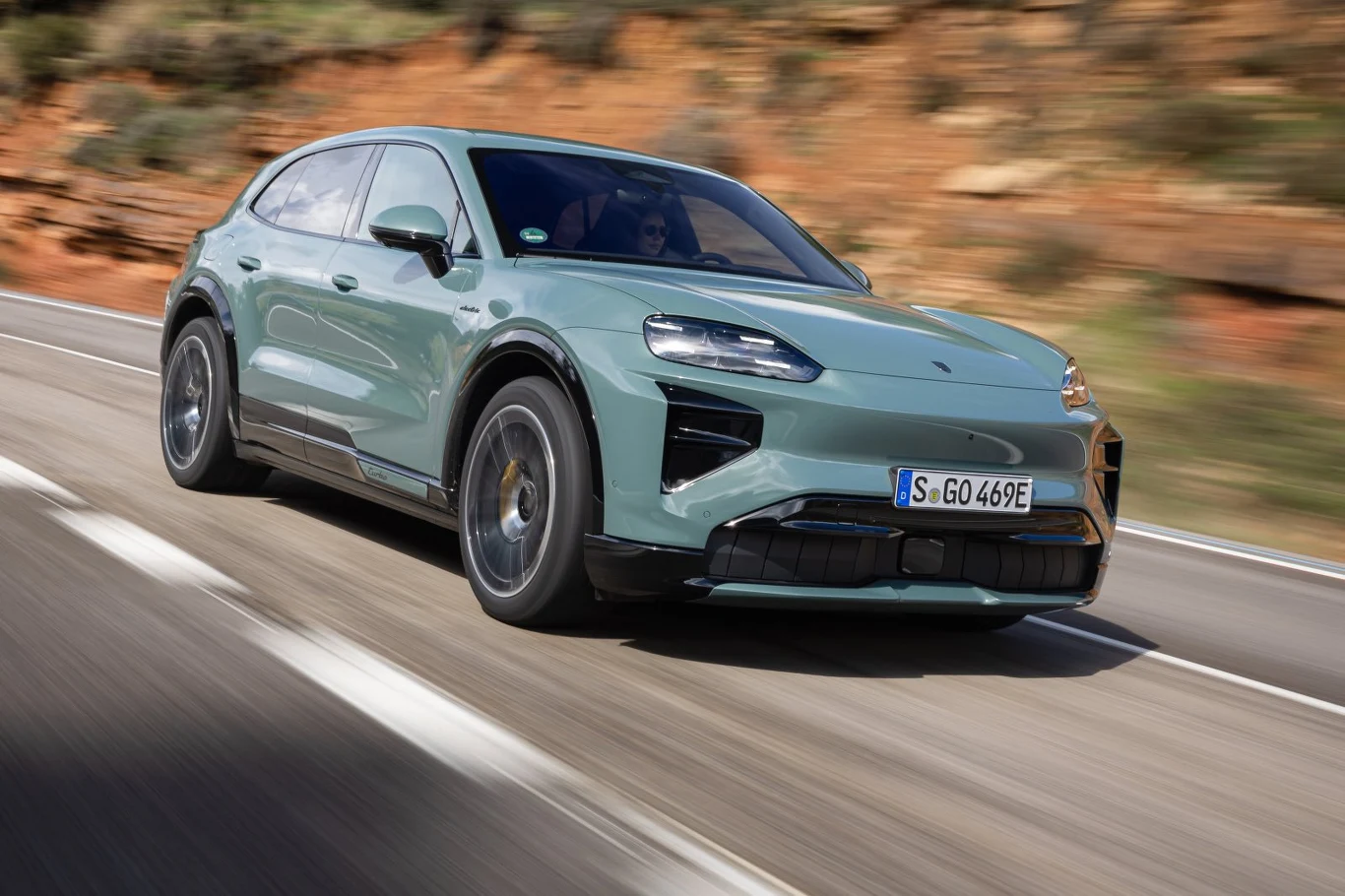 Jasnozielony nowoczesny SUV o sportowej sylwetce porusza się dynamicznie po asfaltowej drodze, na tle skalistego, brązowego krajobrazu.