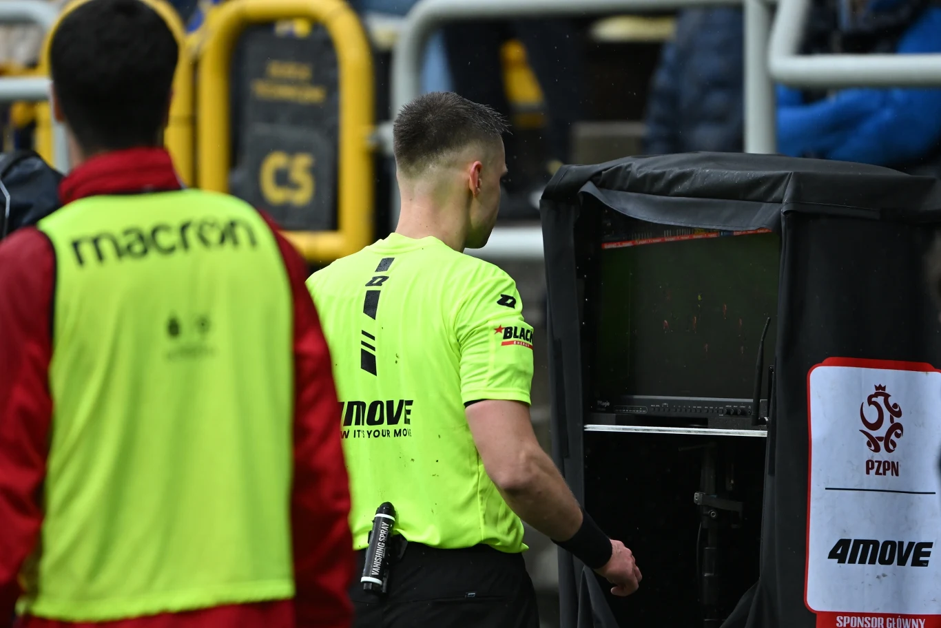 sędzia piłkarski w żółtej koszulce analizuje sytuację meczową przy monitorze VAR podczas meczu piłkarskiego