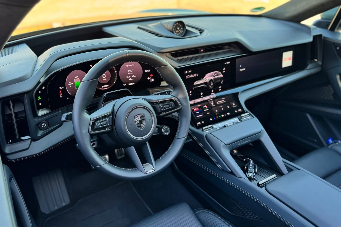 kokpit luksusowego samochodu z cyfrowymi wyświetlaczami, nowoczesną kierownicą z logo Porsche, dotykowym panelem sterowania i eleganckim, minimalistycznym wnętrzem