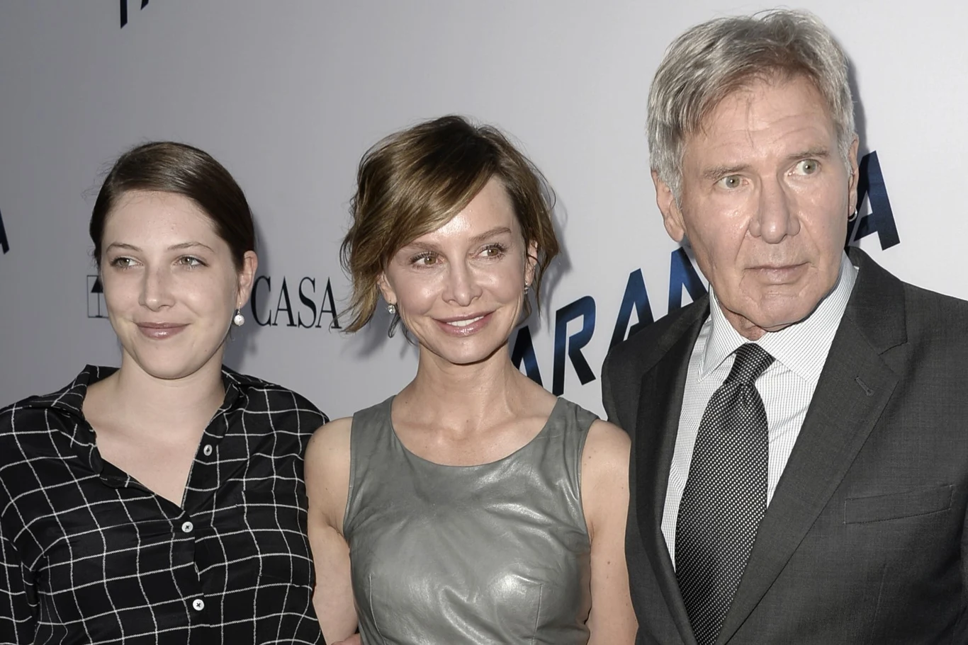 Trzy osoby pozują razem na tle ścianki z napisami; kobieta po lewej ma ciemne, spięte włosy i koszulę w kratę, kobieta w środku ma krótkie, jasnobrązowe włosy i szarą sukienkę bez rękawów, mężczyzna po prawej ma siwe włosy, nosi szary garnitur, białą k...