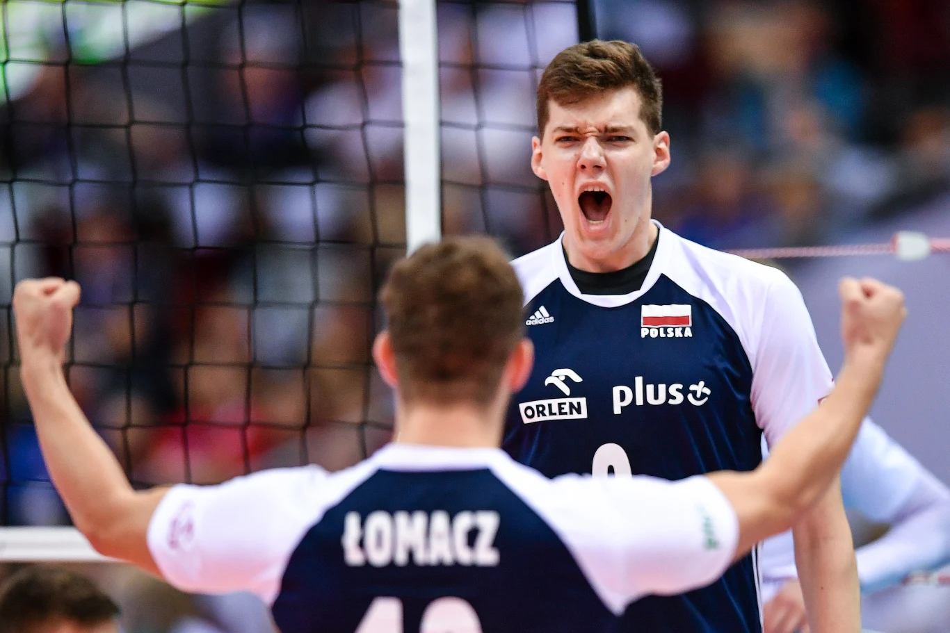 dwóch siatkarzy reprezentacji Polski w sportowych koszulkach okazuje silne emocje podczas meczu, jeden zawodnik z widocznym nazwiskiem łomacz z uniesionymi rękami w geście triumfu, drugi krzyczy z szeroko otwartymi ustami, a w tle widoczna siatka boiska