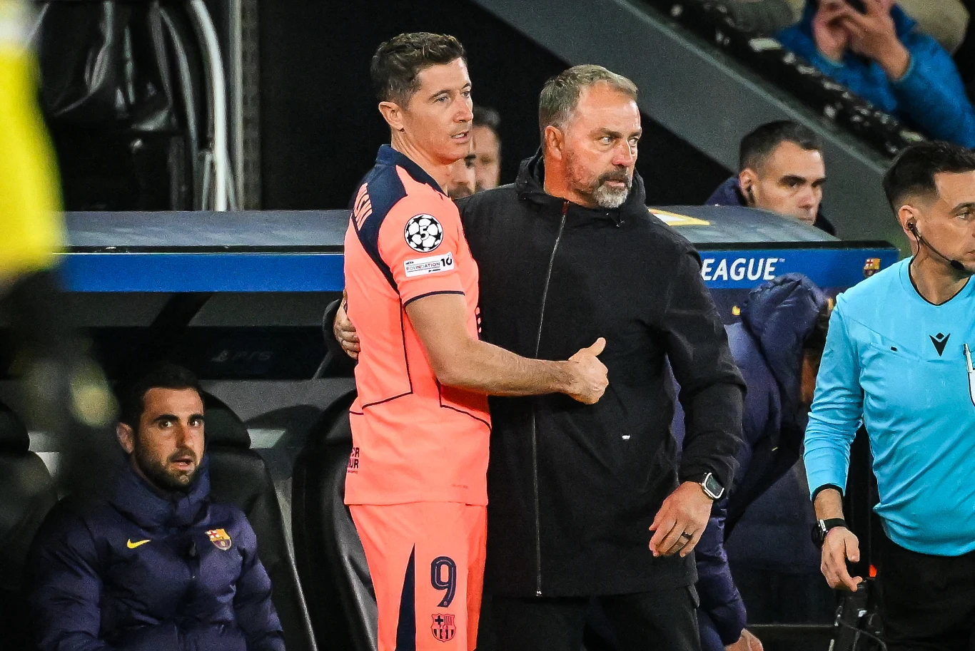 piłkarz w różowym stroju z numerem 9 stoi obok trenera w czarnej kurtce, obaj sprawiają wrażenie, że wymieniają gest wsparcia przy ławce rezerwowych podczas meczu piłki nożnej