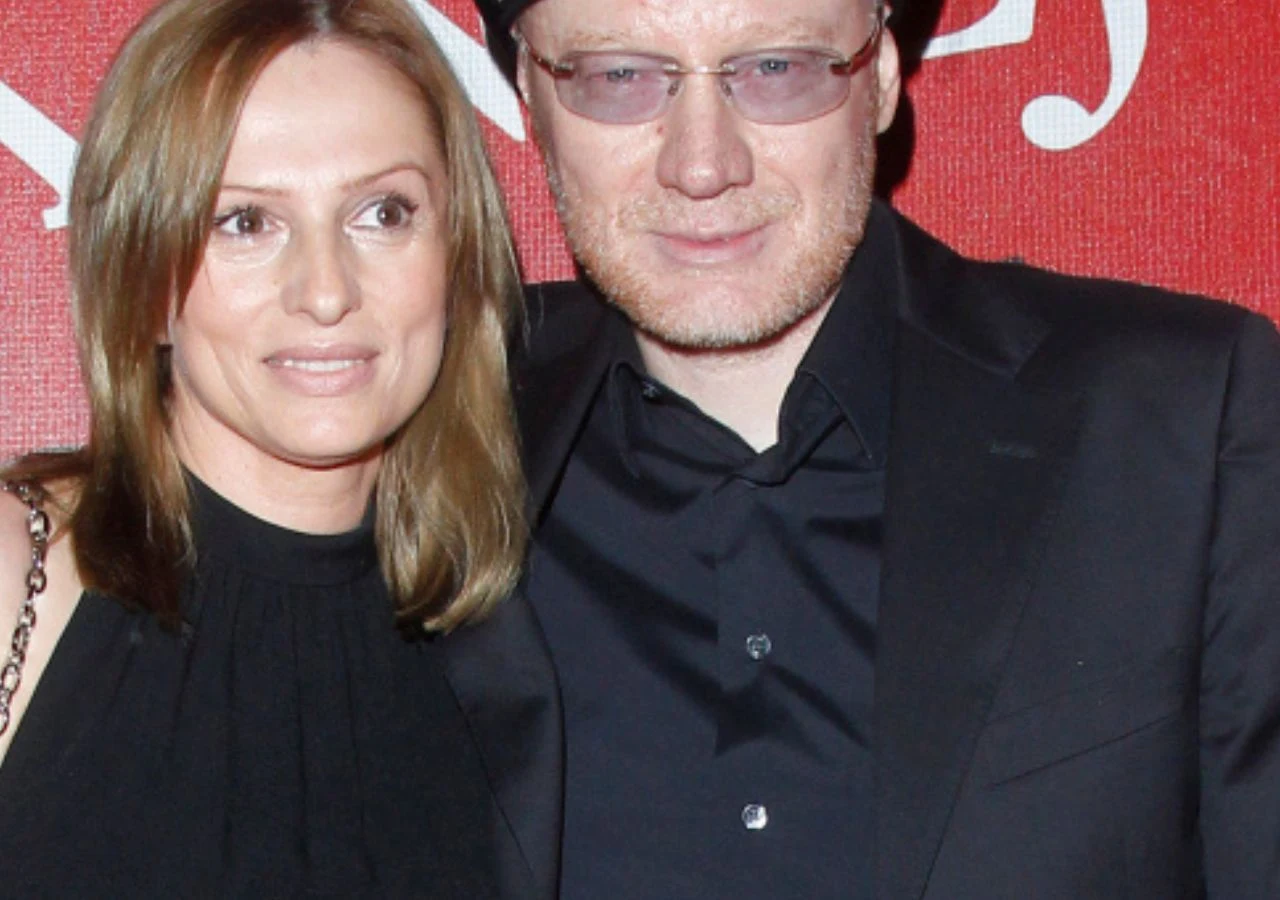 Beata Janson w brązowych włosach i czarnej sukience. Robert Janson w okularach, czarnej koszuli i marynarce. Stoją na czerwonym tle.