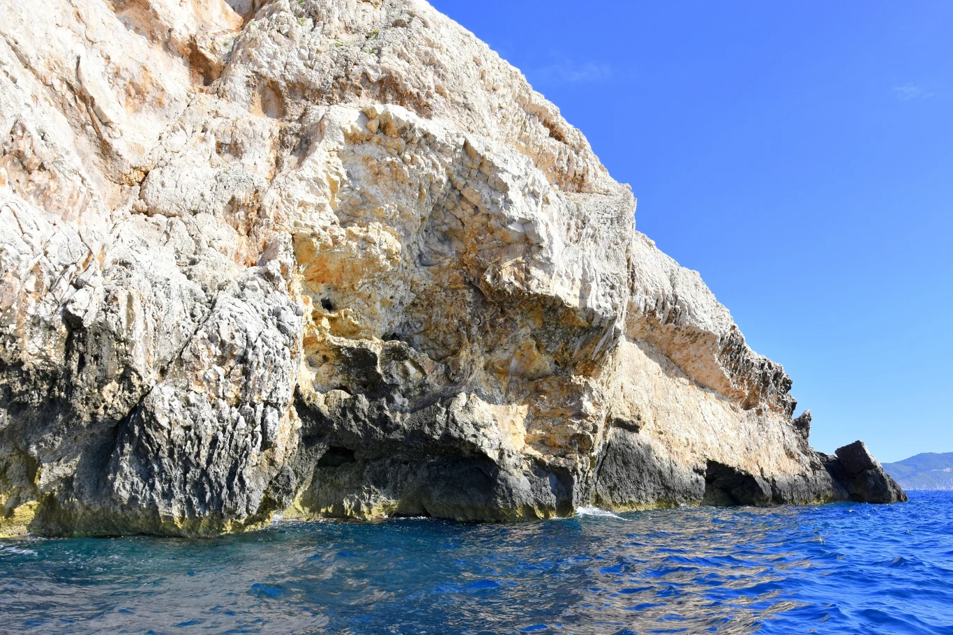 Stroma, jasna skała opadająca bezpośrednio do krystalicznie czystej, błękitnej wody morskiej pod jasnym, bezchmurnym niebem.