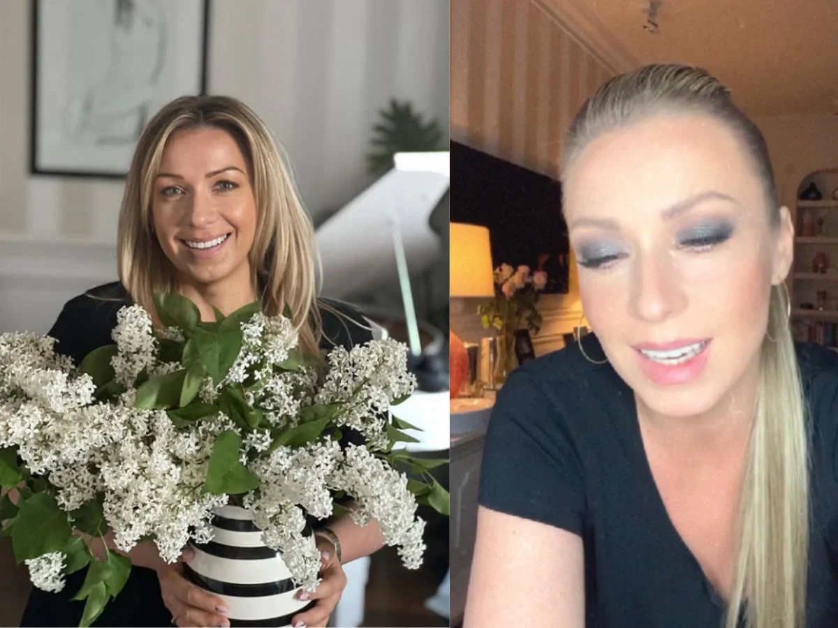 Kobieta z długimi blond włosami trzyma bukiet białych bzów w pasiastym wazonie, obok jej portret z rozpuszczonymi włosami i makijażem, w tle wnętrze mieszkania z dekoracjami i półkami z książkami.