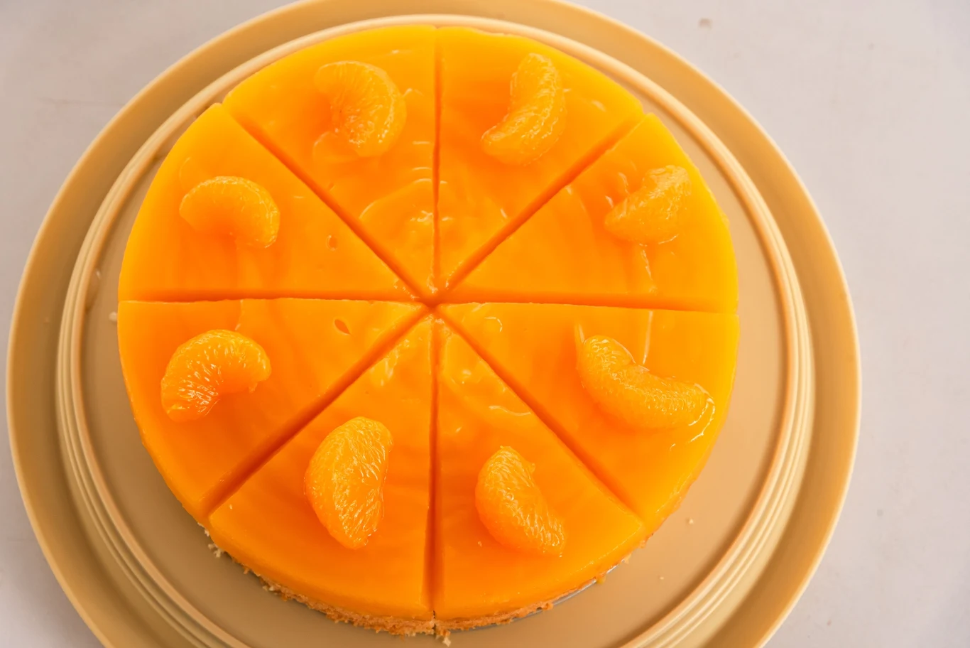 okrągłe ciasto pokryte galaretką pomarańczową, podzielone na osiem równych kawałków, na każdym kawałku położona cząstka mandarynki