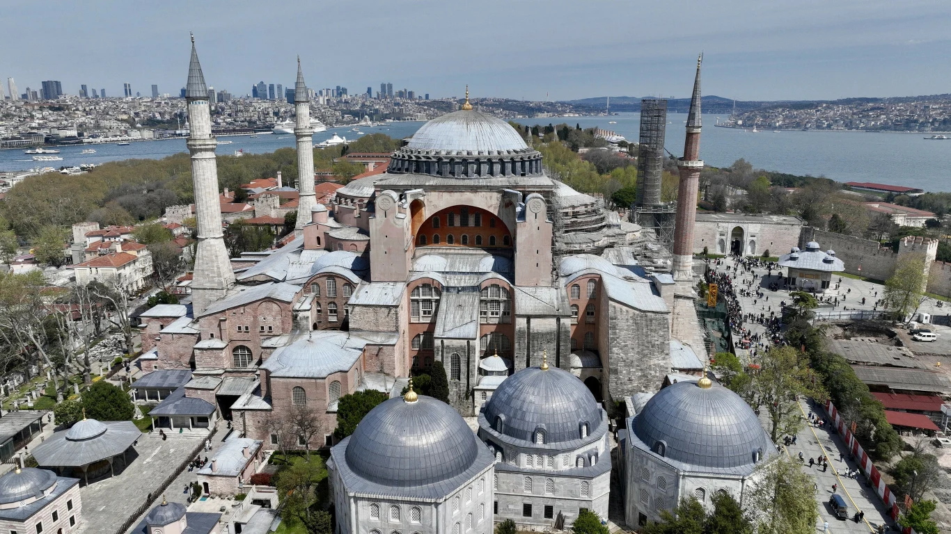 Hagia Sophia z czterema minaretami, monumentalna kopuła w centrum, otoczenie zieleni i zabudowa miejska w tle, w oddali widoczny Bosfor i panorama Stambułu.