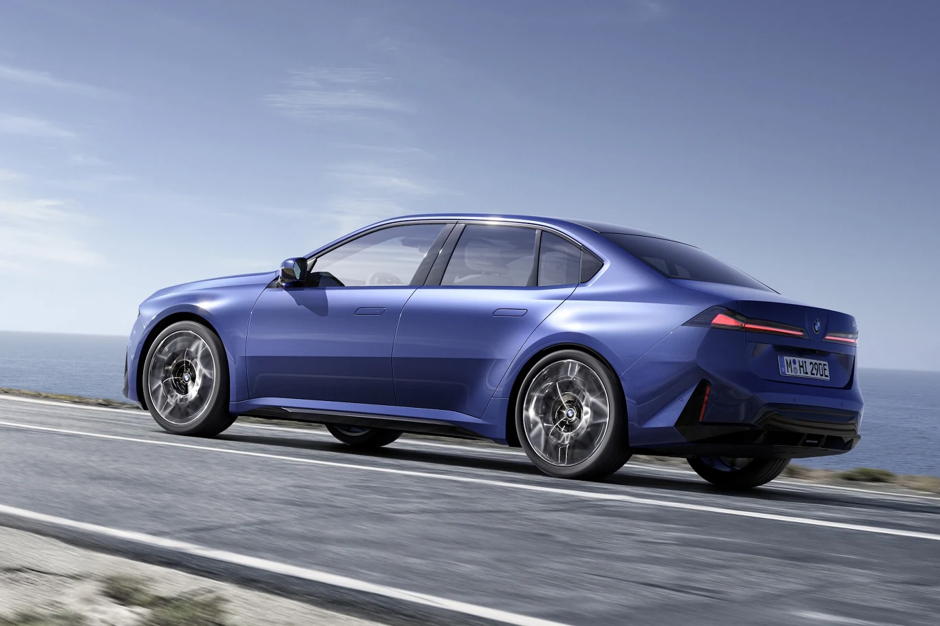 niebieski, luksusowy sedan jedzie dynamicznie wzdłuż wybrzeża, podkreślając sportową sylwetkę, masywne felgi i nowoczesne tylne światła LED