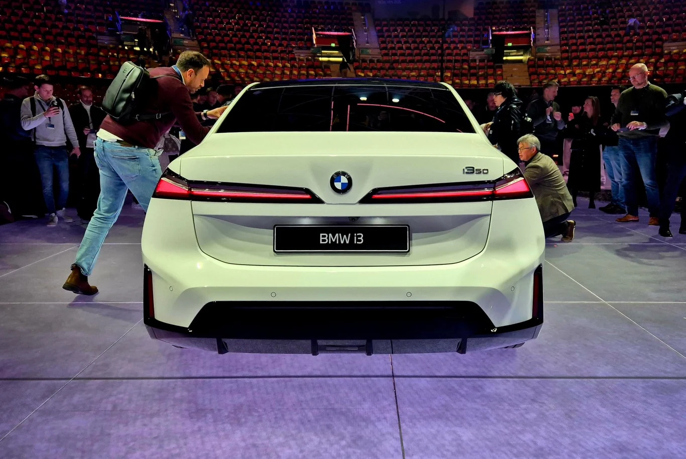 biały samochód BMW i3 pokazany od tyłu na targach motoryzacyjnych, otoczony przez grupę zainteresowanych osób robiących zdjęcia i oglądających pojazd
