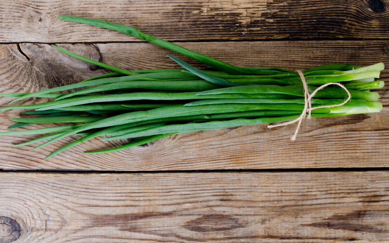 Pęczek świeżego szczypiorku związany sznurkiem, ułożony na drewnianej powierzchni.