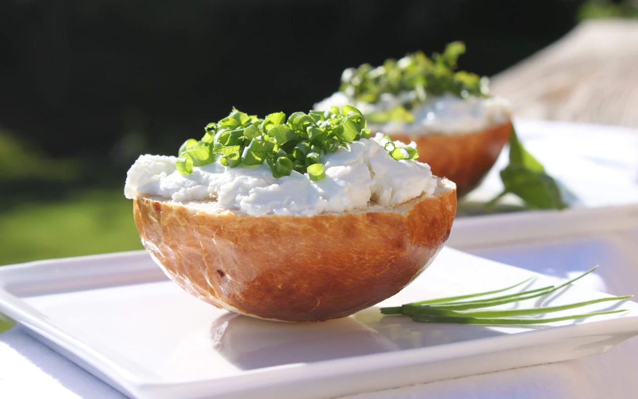 połówka bułki pszennej wypełniona twarogiem i obficie posypana świeżo posiekanym szczypiorkiem, podana na białym talerzu