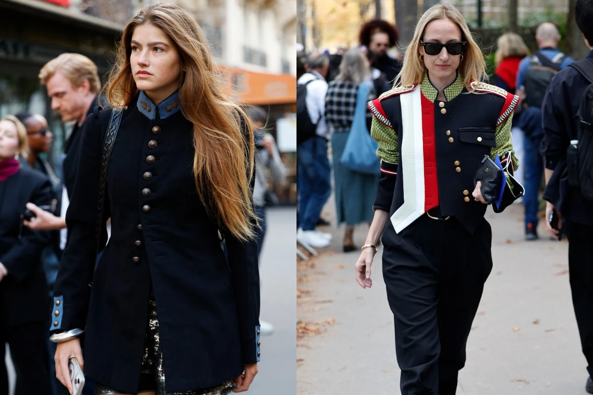 Dwie kobiety ubrane w stylizacje inspirowane militarnymi mundurami, jedna w długim, ciemnym płaszczu z dekoracyjnymi guzikami i niebieskimi akcentami, druga w czarnej kurtce z czerwonymi i zielonymi elementami oraz wyróżniającą się białą tasiemką na ra...