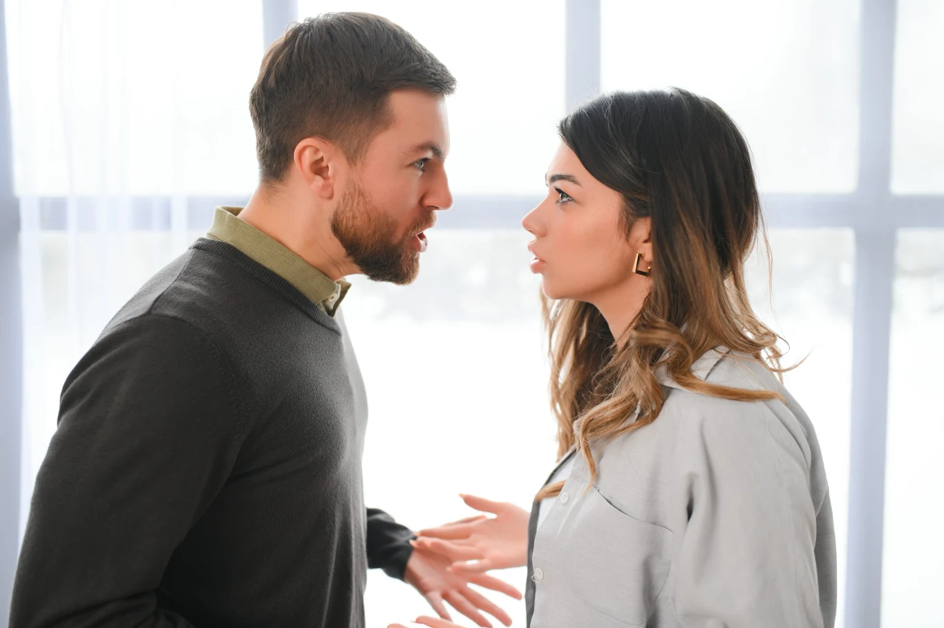 Mężczyzna i kobieta stoją naprzeciw siebie, intensywnie rozmawiając; na ich twarzach widoczne są emocje, które mogą sugerować kłótnię lub poważną wymianę zdań.