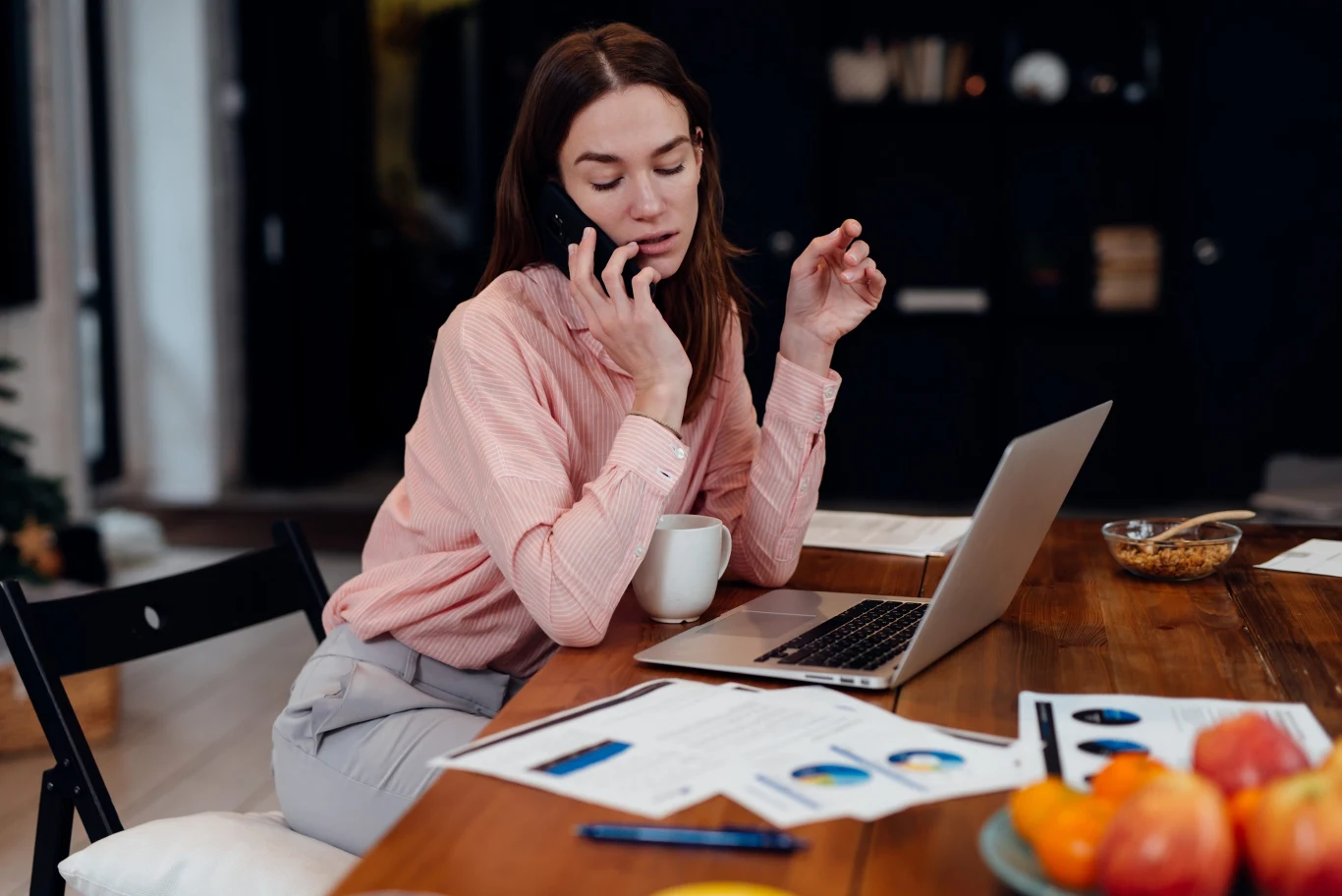 Praca zdalna całkowicie zmieniła rynek zatrudnienia Kobieta pracuje zdalnie przy stole z laptopem, dokumentami, wykresami i talerzem z owocami.