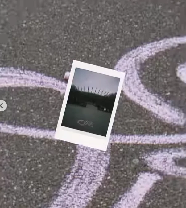 Polaroidowa fotografia z widokiem stadionu leży na asfalcie, na którym namalowano białą linię tworzącą duży symbol nieskończoności.