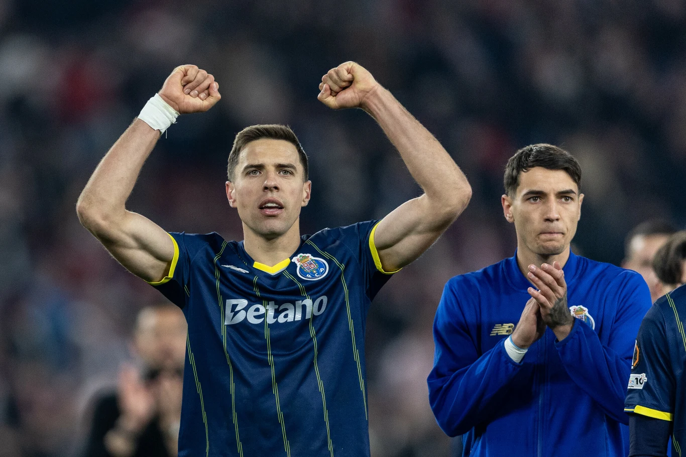 Jan Bednarek w granatowej koszulce z uniesionymi rękami i Jakub Kiwior w niebieskiej kurtce na tle kibiców