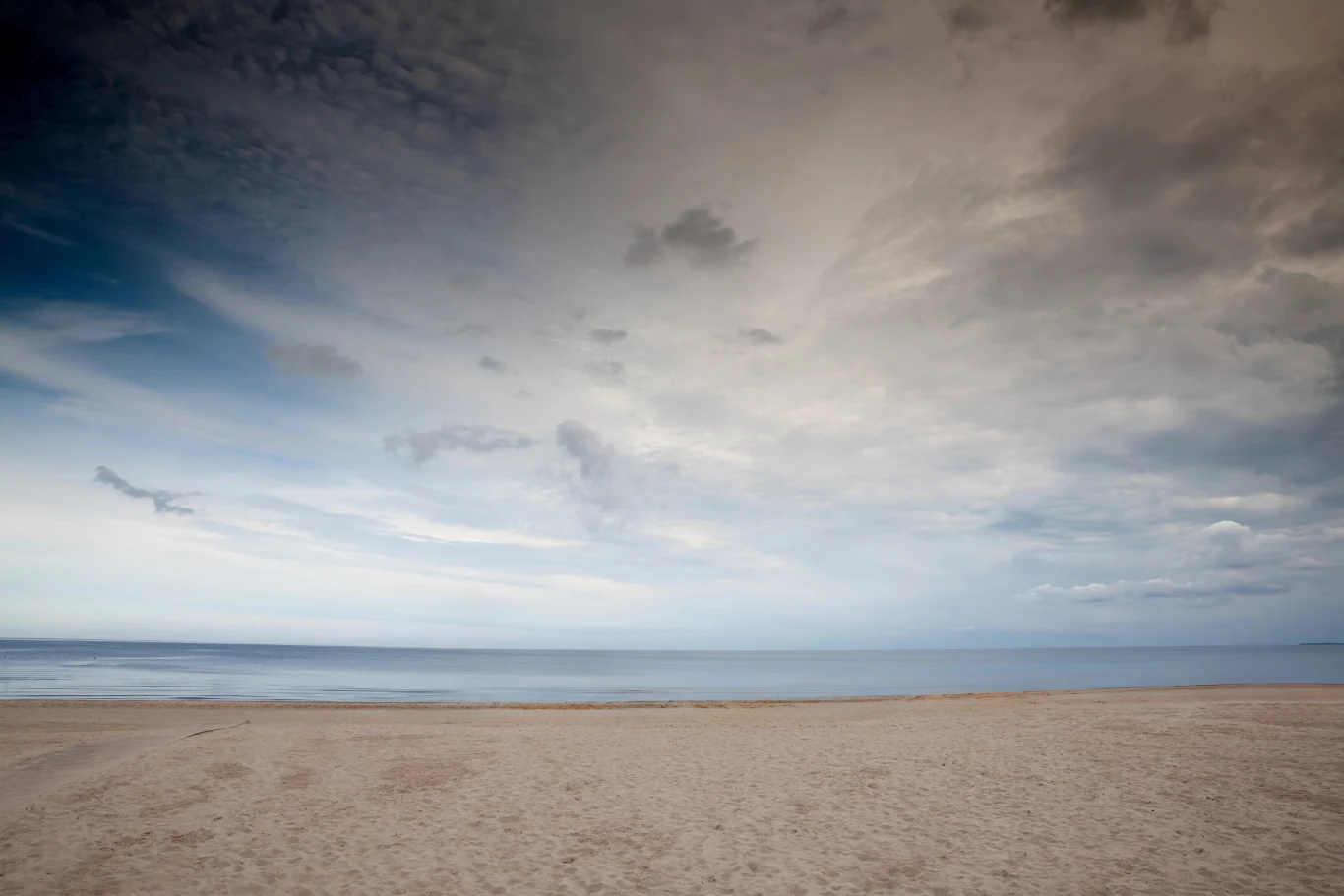 pusta, szeroka plaża z delikatnie wzburzonym morzem pod rozległym, pochmurnym niebem