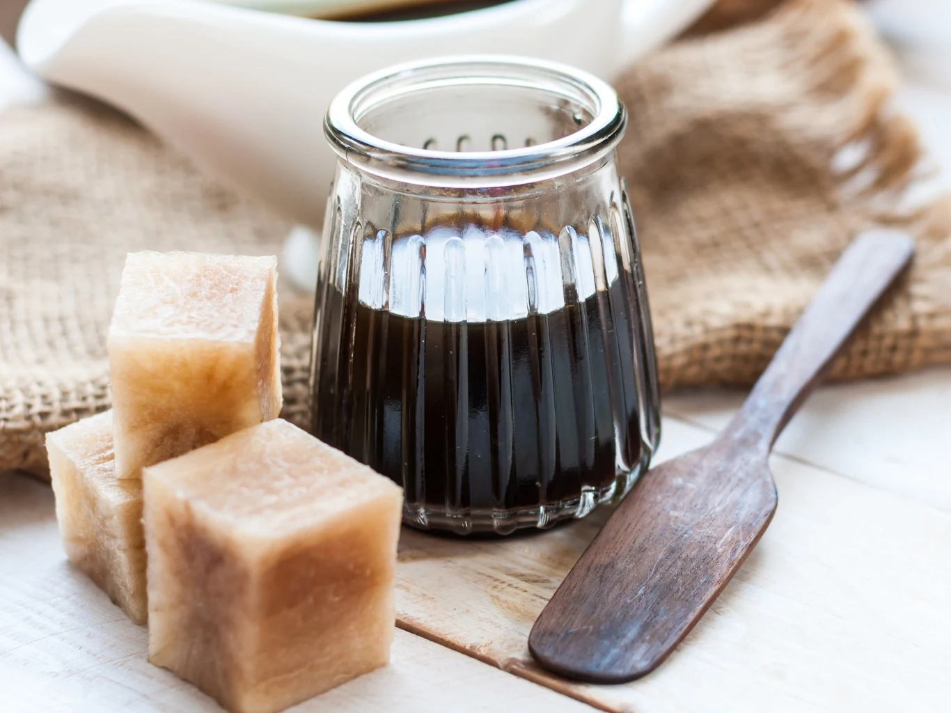 To jeden z najzdrowszych zamienników białego cukru. Sprawdzi się do kawy, ciast i deserów Syrop przygotowany z yaconu w szklanej buteleczce. Obok drewniana łyżka i kostki świeżej bulwy.