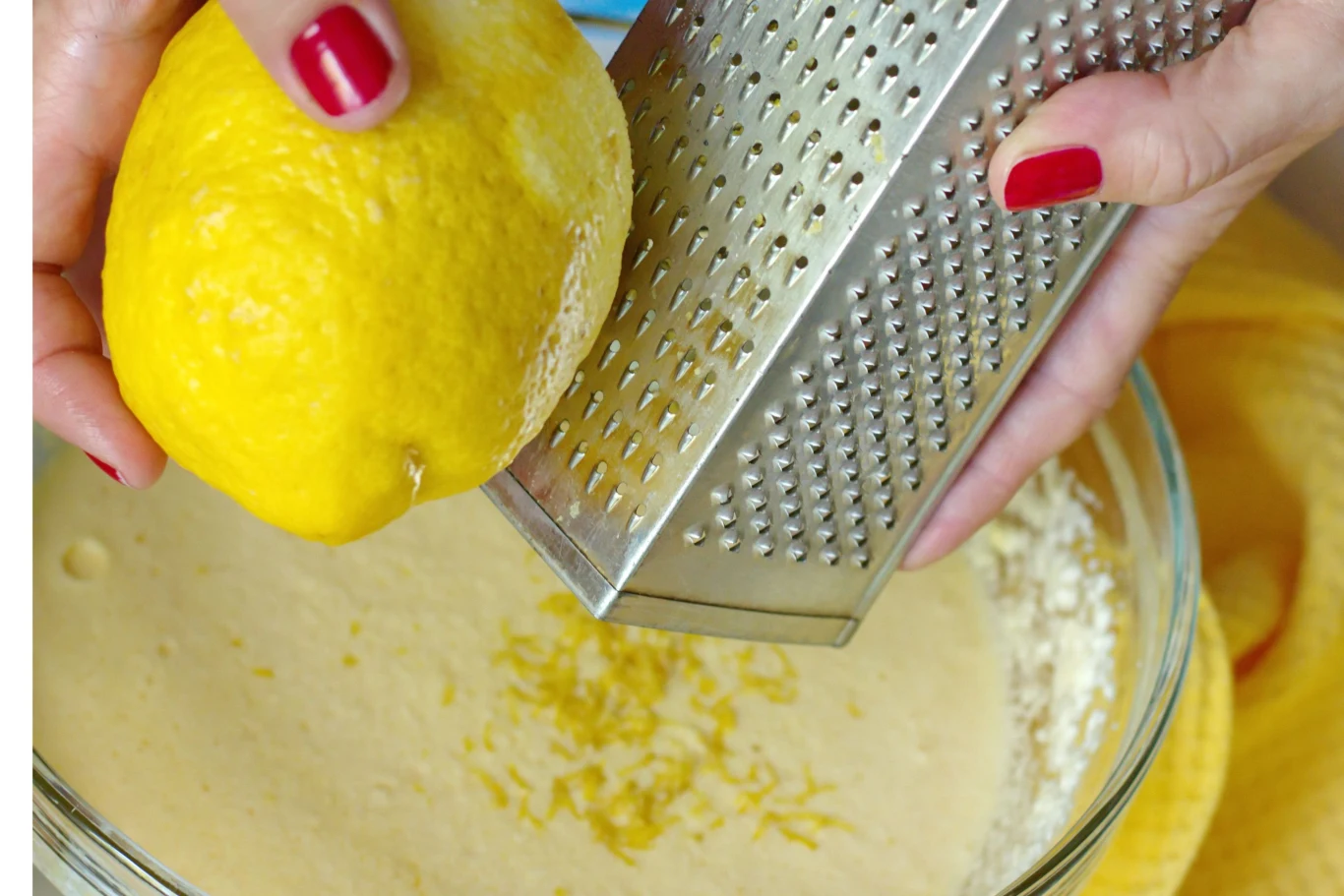 ręka z czerwonym lakierem do paznokci ściera skórkę z cytryny na tarce bezpośrednio do miski z jasną masą